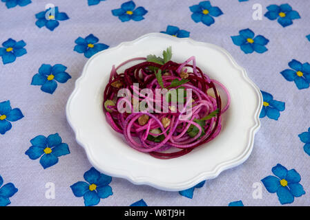 Gesunde imitation Nudeln mit spiralized Rüben, mit Koriander Blätter und Muttern eingerichtet, auf weiße Platte, auf der mit weißen Tischtüchern dekoriert mit Blu Stockfoto