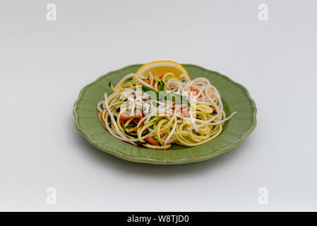 Gesunde imitation Nudeln mit spiralized Zucchini, dekoriert mit basilikumblätter und einer Scheibe Zitrone, auf grüne Platte, Isolated On White Backgroun Stockfoto