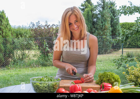 Lächelnd attraktive junge Frau ist Schneiden Tomaten im Freien. Stockfoto