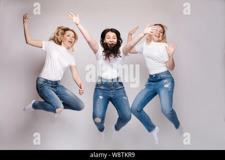 Drei Freunde in legere Kleidung tanzen und springen. Verschiedene, aber schöne Frauen in Jeans und weißen T-Shirts Spaß, und lächelnd. Glückliche junge Stockfoto