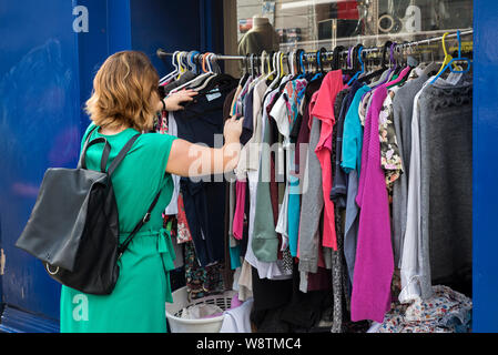 Eine junge Frau rummages durch ein Rack mit gebrauchter Kleidung außerhalb einer Charity Shop auf Nicolson Street, Edinburgh, Schottland, Großbritannien. Stockfoto