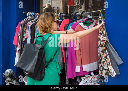 Eine junge Frau rummages durch ein Rack mit gebrauchter Kleidung außerhalb einer Charity Shop auf Nicolson Street, Edinburgh, Schottland, Großbritannien. Stockfoto