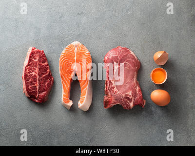 Carnivore oder keto Diät Konzept. Zutaten für Zero carb oder Low Carb Diät - Rib Eye Steak, Lachs, Schweinefleisch, Eier auf grauem Stein Hintergrund. Top View oder flach. Stockfoto