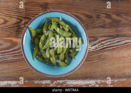 Gesalzene Edamame in blauer Schüssel auf Holz- Hintergrund Stockfoto