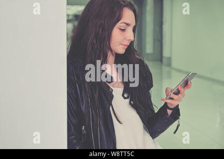 Ein schönes Mädchen verwendet ein Smartphone in einem Bürogebäude lehnte sich gegen eine Wand geschossen mit Copyspace Stockfoto