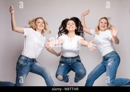 Drei Freunde in legere Kleidung tanzen und springen. Verschiedene, aber schöne Frauen in Jeans und weißen T-Shirts Spaß, und lächelnd. Glückliche junge Stockfoto