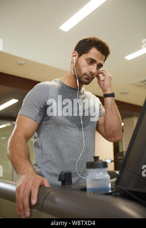Taille bis Portrait von schwitzenden Jungen Mann hören von Musik während der Ausführung auf Laufband im Fitnessstudio Stockfoto