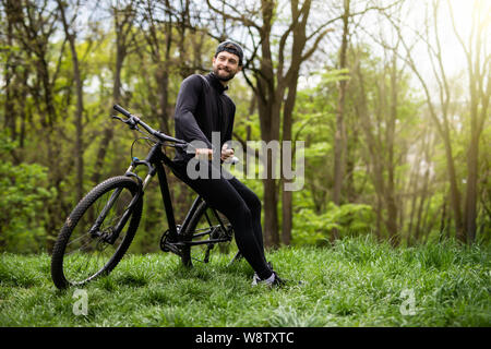 Radfahrer in Shorts und Jersey auf eine moderne Carbon hardtail Fahrrad mit einem Luftgefederten Gabel steht auf einer Klippe vor dem Hintergrund des frischen grünen Su Stockfoto