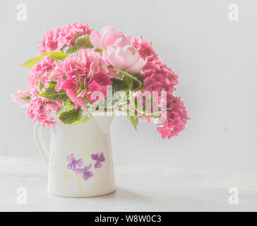 Hortensien und Rosen in einer verzierten Kanne. Stockfoto