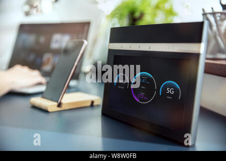 Modernes 5-G WLAN-Router mit Display am Schreibtisch und Geräte im Hintergrund. Schnittstelle auf dem Bildschirm war im Grafik Programm erstellt. Stockfoto