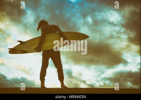 Sonnenuntergang Silhouette einer surfer Holding sein Surfbrett vor dramatischen skyscape Stockfoto