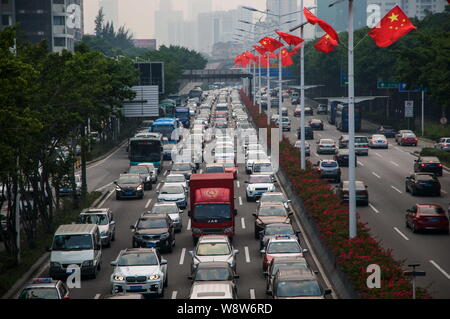 Massen von Fahrzeugen bewegen sich langsam in einem Stau an einer Straße mit chinesischen nationalen Flaggen dekorierte der Nationale Tag Urlaub in Shenzhen City zu feiern. Stockfoto