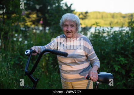 Ältere Frau mit dem Fahrrad einen Außenpool. Rentner die Fahrt mit dem Fahrrad. Stockfoto