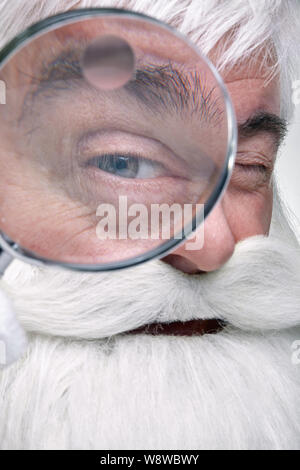 Nahaufnahme des Gesichts des Santa Claus. Weißhaariger alter Mann mit weißem Bart und Schnurrbart in der Kamera durch ein Vergrößerungsglas Stockfoto