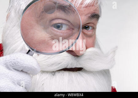 Nahaufnahme des Gesichts des Santa Claus. Weißhaariger alter Mann mit weißem Bart und Schnurrbart in der Kamera durch ein Vergrößerungsglas Stockfoto