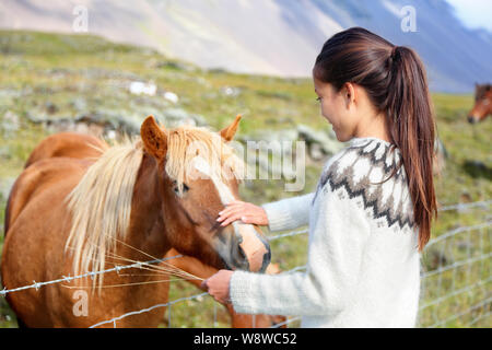 Islandpferde - Frau petting Pferd auf Island. Mädchen in Pullover gehen Reiten lächelt glücklich mit Pferd, in schöner Natur auf Island. Stockfoto