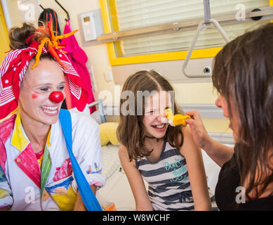 Wiesbaden, Deutschland. 27 Juni, 2019. Dr. Krümel (L-R), Clown Doktor, macht Emma und Mutter Manuela lachen. Der Verein "die Clown Doktoren e.V. ist ein Verband für professionelle Clowns in Krankenhäusern und Pflegeheimen arbeiten bundesweit. Die Akteure versuchen, die betroffenen Menschen Hoffnung zu geben und den Mut, wieder zu Leben durch Humor. Die Clown Doktoren sind auch aktiv in der Kinderklinik der Dr.-Horst-Schmidt-Kliniken. Credit: Andreas Arnold/dpa/Alamy leben Nachrichten Stockfoto