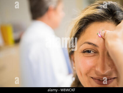 Wiesbaden, Deutschland. 27 Juni, 2019. Aysun, Medical Assistant (MFA), erhält einen Aufkleber auf der Stirn von der Clown Doktor stecken. Der Verein "die Clown Doktoren e.V. ist ein Verband für professionelle Clowns in Krankenhäusern und Pflegeheimen arbeiten bundesweit. Die Akteure versuchen, die betroffenen Menschen Hoffnung zu geben und den Mut, wieder zu Leben durch Humor. Die Clown Doktoren sind auch aktiv in der Kinderklinik der Dr.-Horst-Schmidt-Kliniken. Credit: Andreas Arnold/dpa/Alamy leben Nachrichten Stockfoto