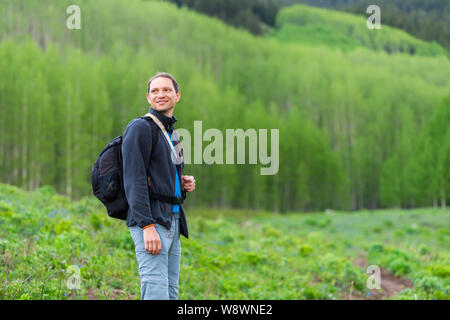 Mann lächelnd zurück Suchen mit Rucksack auf Snodgrass Trail mit bokeh Hintergrund Blick von Aspen Wald in Mount Crested Butte, Colorado in Summ Stockfoto