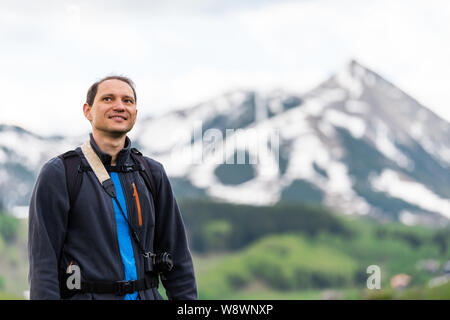 Mann lächelnd auf Snodgrass Trail mit Kamera und bokeh Hintergrund Blick auf Mount Crested Butte, Colorado Peak und Dorf im Sommer Stockfoto