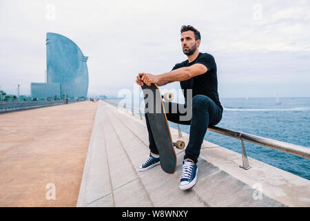 Skateboarder sitzt mit Skateboard auf die moderne Stadt Meer Terrasse Stockfoto