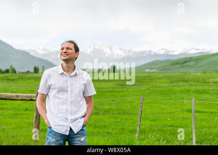 Crested Butte, Colorado Land mit glücklichen jungen Mann durch Zaun und im Sommer auf bewölkten Tag mit grünem Gras und Blick auf die Berge Stockfoto