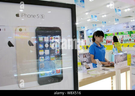 ---- Ein Mitarbeiter ist neben einer Werbung für iPhone 5S Smartphones von Apple zu einem Handy store in Beijing City, South China Hainan pr gesehen Stockfoto