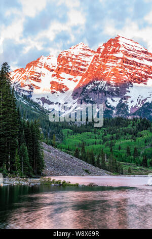 Maroon Bells red sunrise Light Peak vertikale Ansicht in Aspen, Colorado während der Blauen Stunde bewölkten Himmel und Schnee im Frühsommer Stockfoto