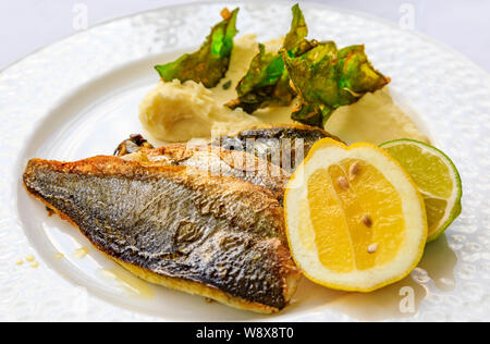 Pfanne gebratene Branzino oder Wolfsbarsch mit Zitrone und Limette Keile serviert und Kartoffelpüree mit gebratenen kale Chips bei einer al fresco Restaurant in Montenegro Stockfoto