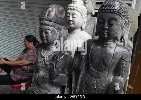 Ein chinesischer Hersteller sitzt neben Buddha Statuen zum Verkauf an der Shanghai Dongtai Road Antique Market in Shanghai, China, 18. August 2014. Ein Antiquitäten st Stockfoto