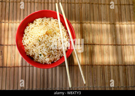 Asiatische Nudeln in eine rote Tasse mit Stäbchen. Gegen einen Bambus Matte. Stockfoto