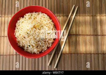 Asiatische Nudeln in eine rote Tasse mit Stäbchen. Gegen einen Bambus Matte. Die Aussicht von oben. Stockfoto