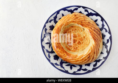 Die traditionellen Zentralasiatischen Brot, tandoor Pellet. Auf einem nationalen Stil Teller. Weiße strukturierte Hintergrund. kopieren. Stockfoto