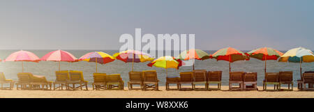 Horisontal Banner-Reihe von leeren Holz- Chaiselongue mit bunten Schirme am Strand in Goa, Indien, getönt mit Sonnenlicht. Meer Sommerurlaub bac Stockfoto