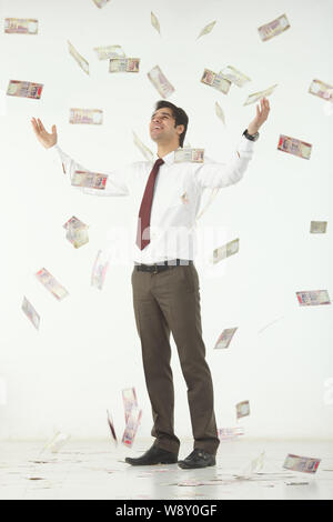 Geld fällt auf einen Geschäftsmann, der mit ausgestreckten Armen steht Stockfoto