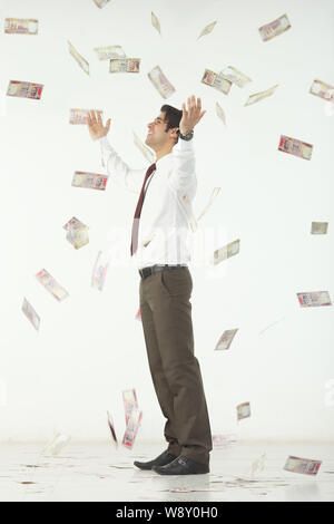 Geld fällt auf einen Geschäftsmann, der mit ausgestreckten Armen steht Stockfoto