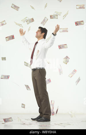 Geld fällt auf einen Geschäftsmann, der mit ausgestreckten Armen steht Stockfoto