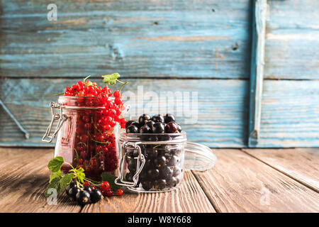 Frische reife Beeren rot Schwarze Johannisbeere verschiedene Gläser Holz- rustikalen Hintergrund. Horizontale Rahmen selektiven Fokus. Stockfoto