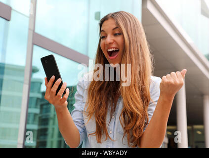 Euphorisch business Frau gerade Ihre Smart Phone und zeigt Sieger Geste outdoor Stockfoto