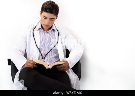 Stattliche Arzt tragen weiße Kittel, im Stuhl sitzen und lesen Taschenbuch auf isolierten Hintergrund. Stockfoto