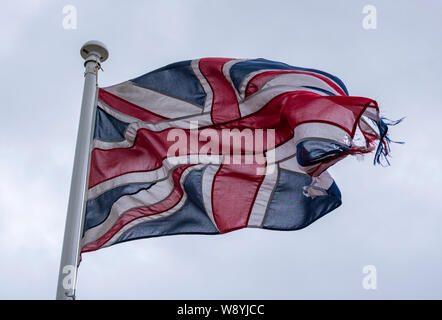 Eine tätbare und zerstückelte gewerkschaftsfahne oder ein britisches Jack Ensign-Emblem, das threadblank und am oberen Ende eines Flagpols im Wind beschädigt wird. Stockfoto