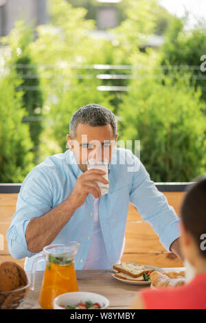 Grauhaarige Mann trinken Milch und hören auf Frau Stockfoto