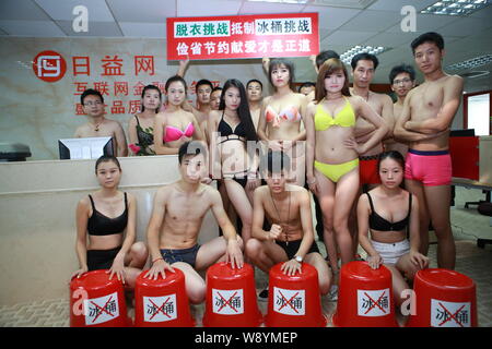 Chinesische Mitarbeiter gekleidet in Bikinis und Badehosen pose hinter leeren Eimer den Eimer für das Eis Herausforderung Boykott in ihrem Büro in Shenzhen cit zu Stockfoto