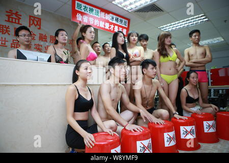 Chinesische Mitarbeiter gekleidet in Bikinis und Badehosen pose hinter leeren Eimer den Eimer für das Eis Herausforderung Boykott in ihrem Büro in Shenzhen cit zu Stockfoto