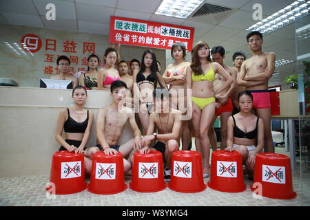 Chinesische Mitarbeiter gekleidet in Bikinis und Badehosen pose hinter leeren Eimer den Eimer für das Eis Herausforderung Boykott in ihrem Büro in Shenzhen cit zu Stockfoto