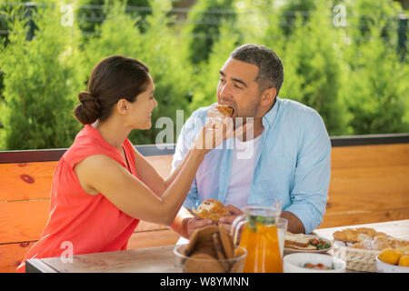 Fürsorgliche Frau lächelnd während einige Croissant geben ihr Mann Stockfoto