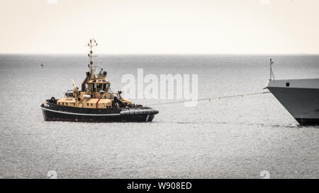 Ein Schubschiff unterstützt die SAS AMATOLA von Simons Town Flottenstützpunkt auf Südafrika der False Bay Küste in der Nähe von Kapstadt Stockfoto