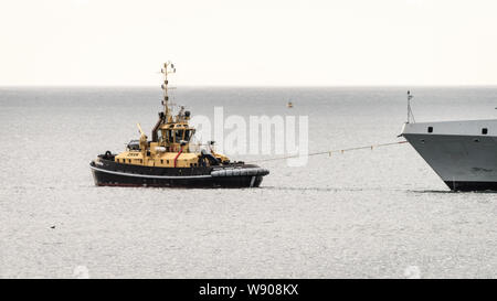 Ein Schubschiff unterstützt die SAS AMATOLA von Simons Town Flottenstützpunkt auf Südafrika der False Bay Küste in der Nähe von Kapstadt Stockfoto