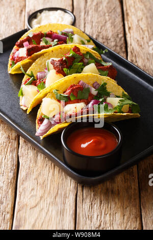 Traditionelle mexikanische Tacos al Pastor mit Schweinefleisch, Ananas, Zwiebeln und Kräuter close-up auf einem Teller auf den Tisch. Vertikale Stockfoto