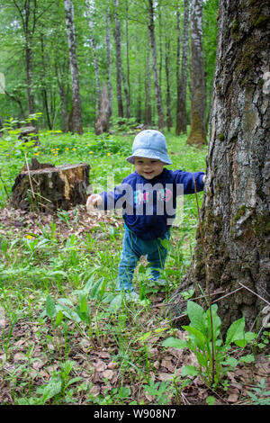 Baby 8-9 Monate lernt laufen, Spaziergänge durch den Wald mit einem Baumstamm. Ein kleines Mädchen lächeln auf einen Spaziergang im Park. Babe in Panama und Jeans enj Stockfoto